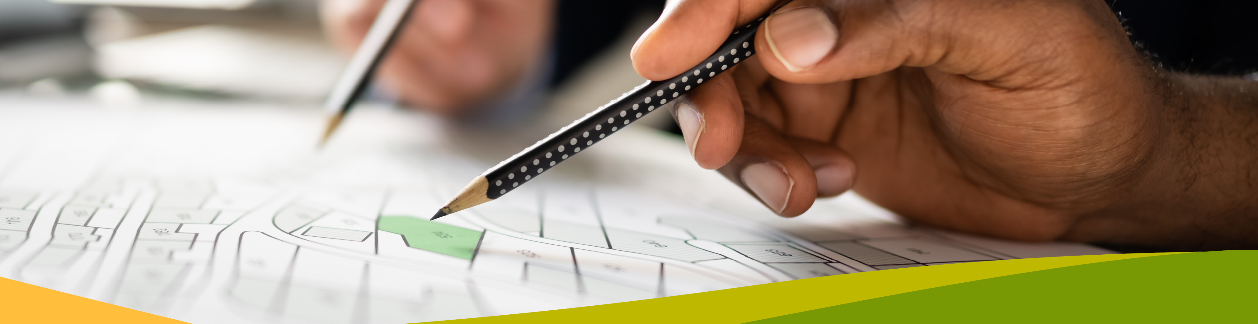 Hand holding pencil above subdivision blueprints.