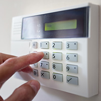 Hand pressing the buttons on a keypad of a home security alarm controller.
