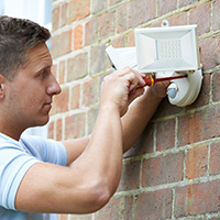Man using screwdriver to install motion activated led floodlight on exterior of home.